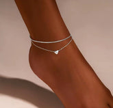 This is a minimalist, silver-plated double-layer ankle bracelet featuring a delicate heart charm and a shimmering chain.