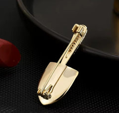 This item is a gold-colored brooch shaped like a shovel, adorned with sparkling crystals.