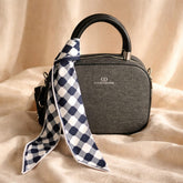 small grey structured handbag with a black top handle and a black and white gingham scarf detail, possibly from the brand Christian Dior