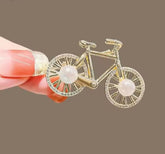 a gold-colored alloy bicycle brooch with faux pearl and rhinestone accents