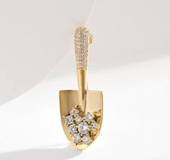 This item is a gold-colored brooch shaped like a shovel, adorned with sparkling crystals.